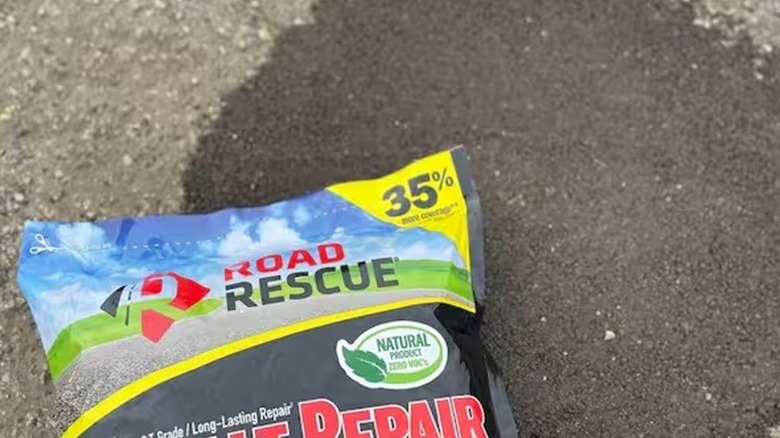 Filled-in pothole in an asphalt driveway with a bag of Road Rescue laying on top.