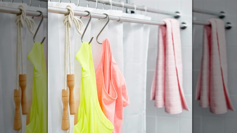 Shower curtain tension rod with s-hooks holding a variety of clothing items and a towel
