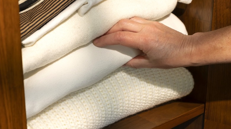 Hand reaches for a cream-colored blanket from a blanket stack in a wooden closet