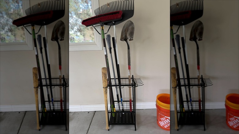 Storage rack against a wall with yard tools standing upright in it