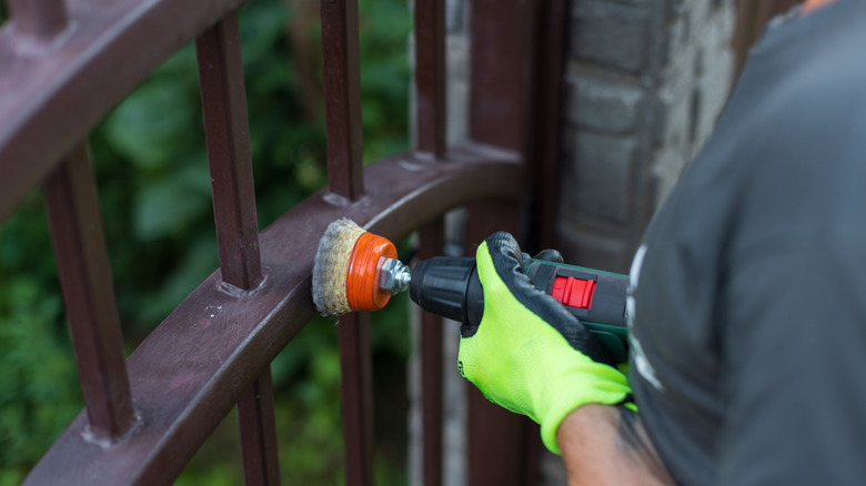Person removing rust from metal gate using brush cup drill attachement