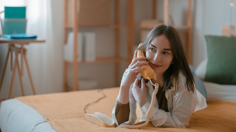 A woman laying on a bed talking on a corded phone