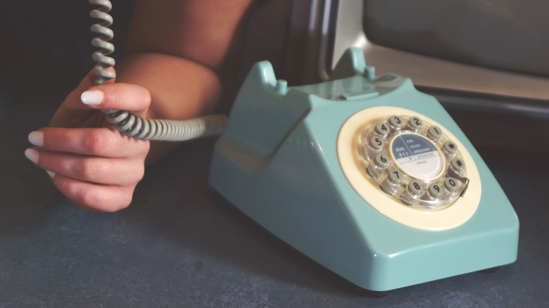 w manicured hand holds the cord of a light blue rotary phone