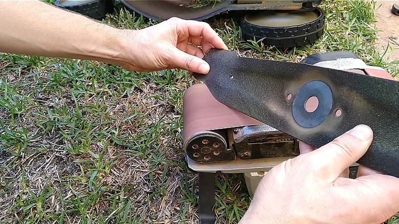 Close-up of a mower blade being sharpened on a stationary belt sander