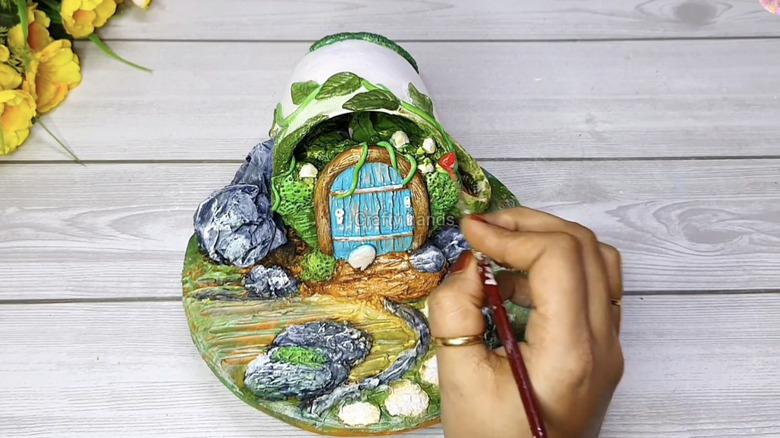 A person adding details to a tea cup fairy home