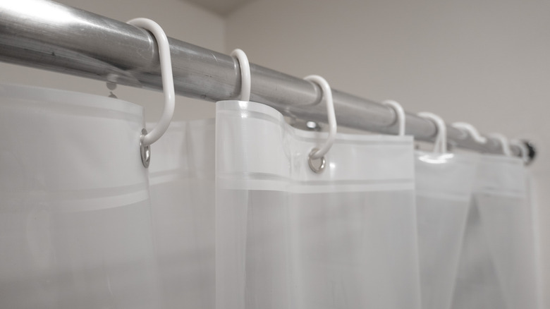 close-up of a clear shower curtain liner hung up by white hooks on a stainless steel curtain rod.