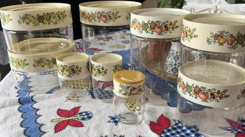 A collection of Pyrex Spice O'Life glass canisters arranged on a table with a patterned tablecloth.