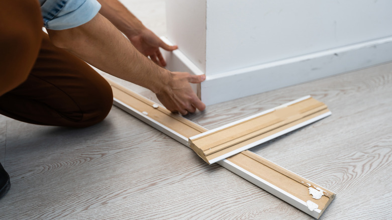 Person installing new baseboards with old baseboards on floor beside them