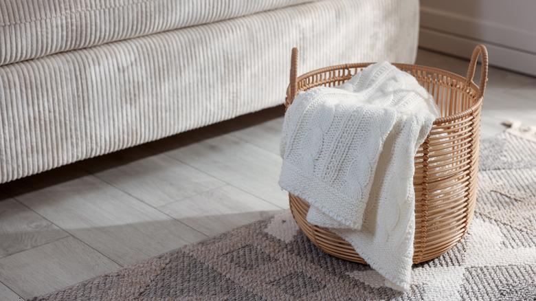 A white woollen blanket draped over the side of an open-weave wicker basket in a living room.