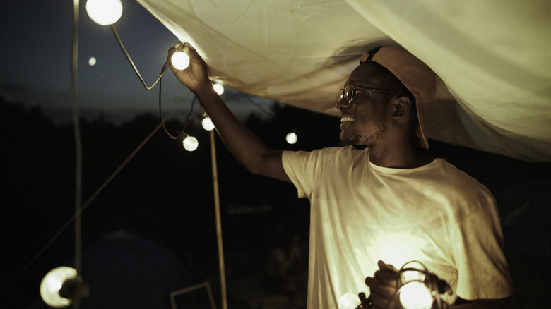 Man hanging string of outdoor lights on tent