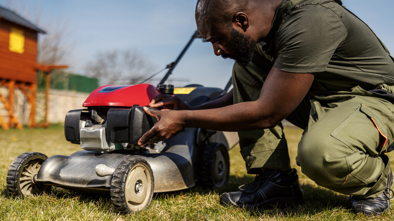 man crouched down looking at lawnmower on lawn