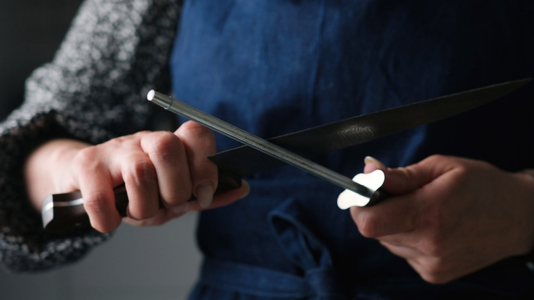 Person In Apron Using A Rod Tool To Sharpen A Large Knife