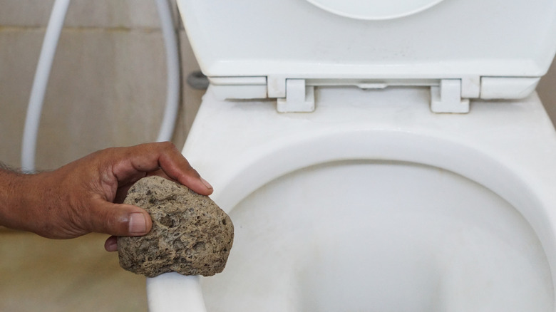 Someone holding a pumice stone near a toilet bowl