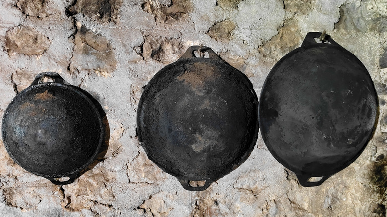 Three cast iron pans hanging on a stone wall