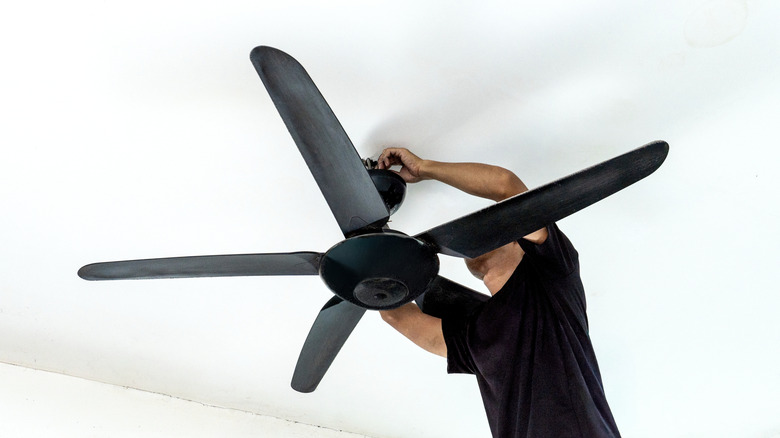 A man installs a black ceiling fan