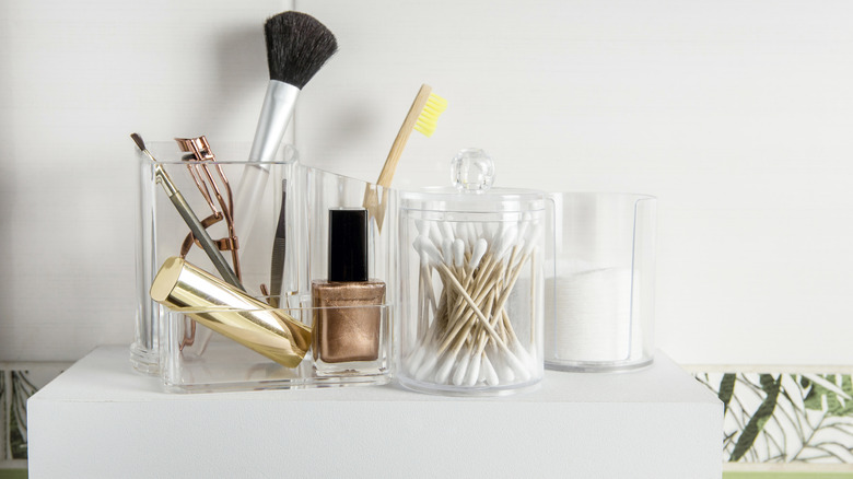 Beauty and hygiene products in acrylic organizers and containers on tidy, minimalist shelf.