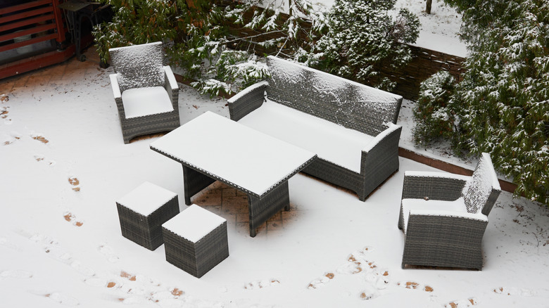 An outdoor sofa, two chairs, two stools, and a table are covered in snow on a patio.