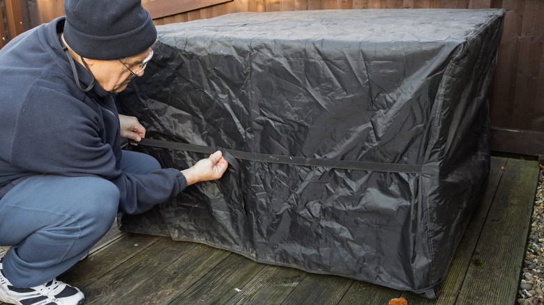 A man tightens a black protective cover on an outdoor table.