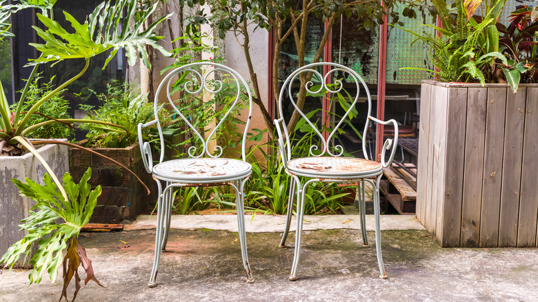 Two rusted white steel outdoor chairs on a patio in a garden.