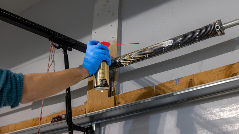 person spraying bottle of wd-40 on garage door springs