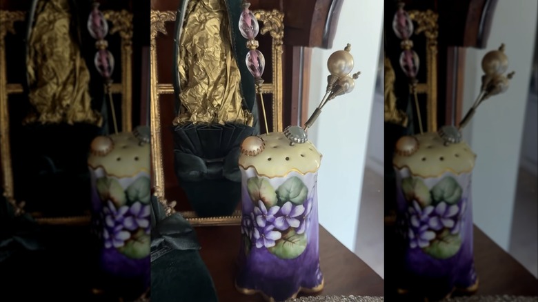 a vintage sugar shaker being used to store and display hat pins in a cabinet