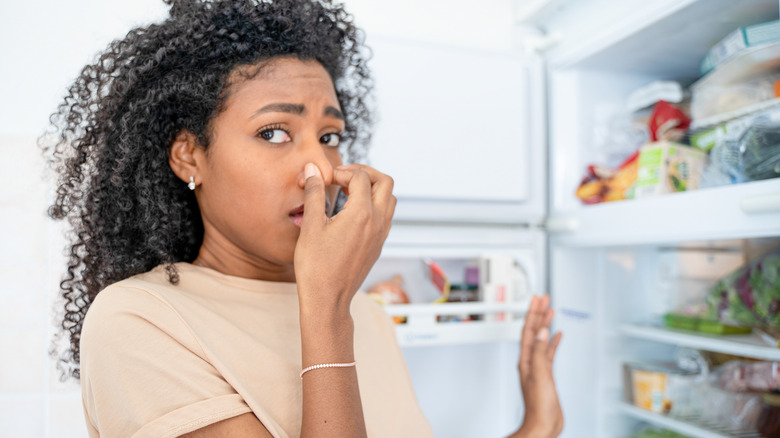 A woman holding her nose while going into the fridge and freezer