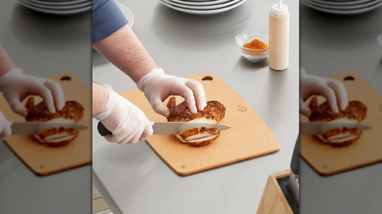 Person cutting fried chicken on composite cutting board