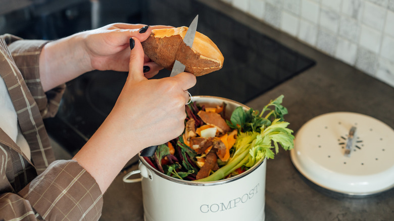 Woman putting vegetables and leftovers into a compost bin on the kitchen table.