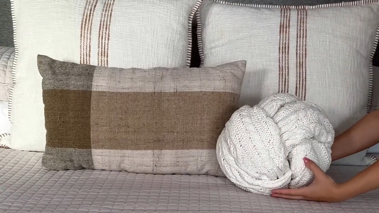 Person placing blanket tied into a knotted pillow on a bed
