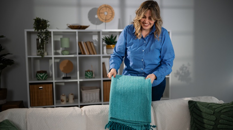 Woman draping folded blue blanket on couch