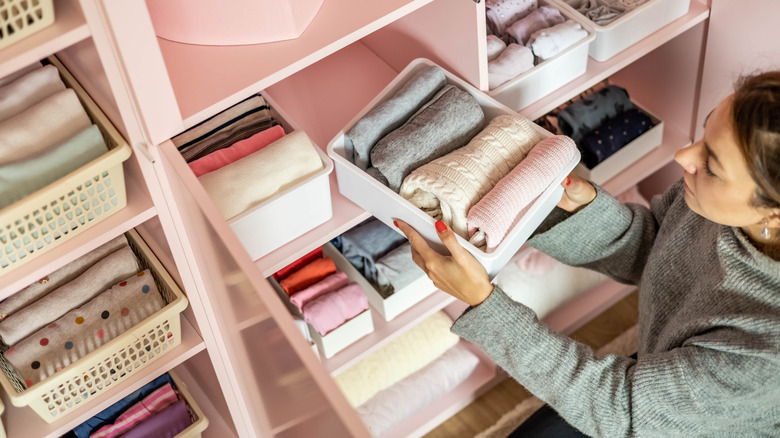 A woman organizing a deep shelf in a closet cabinet with baskets.