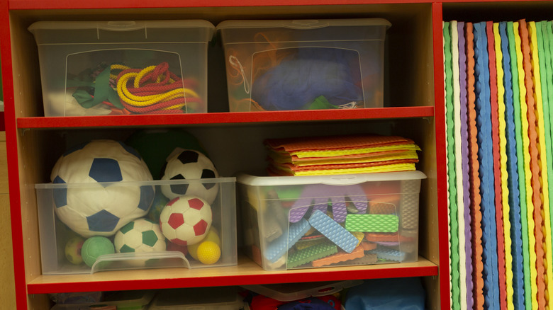 Toys inside plastic bins on red shelves.