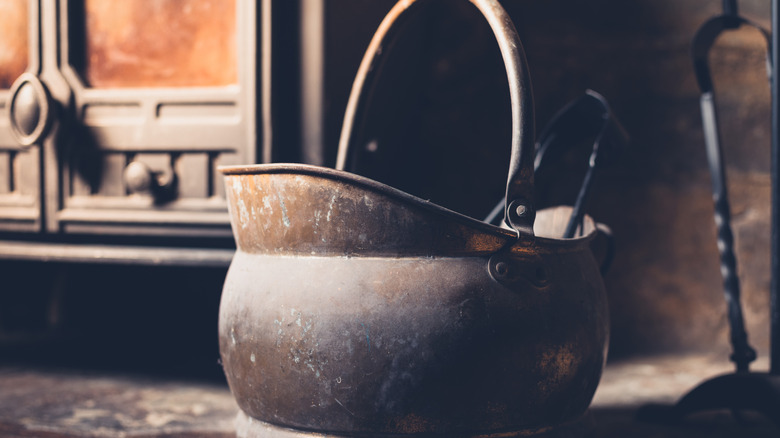 Close up of a an iron coal scuttle next to a wood stove