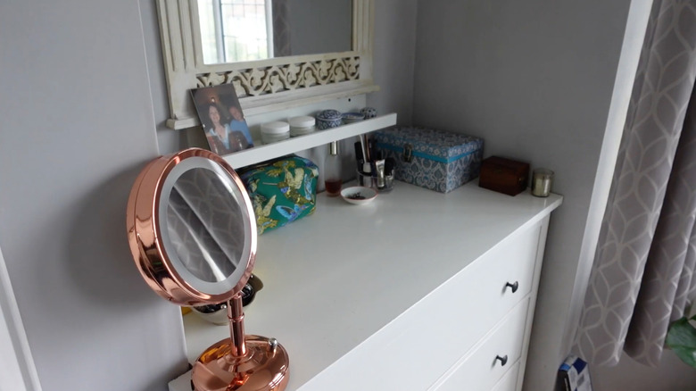 A picture ledge installed above a dresser in a bedroom is used for makeup storage.