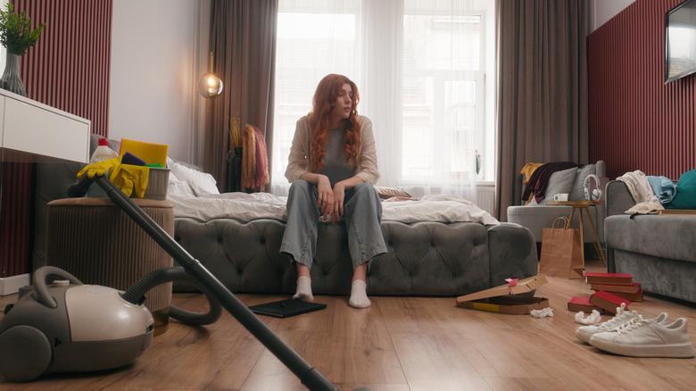 A woman overwhelmed by clutter in a bedroom without a closet