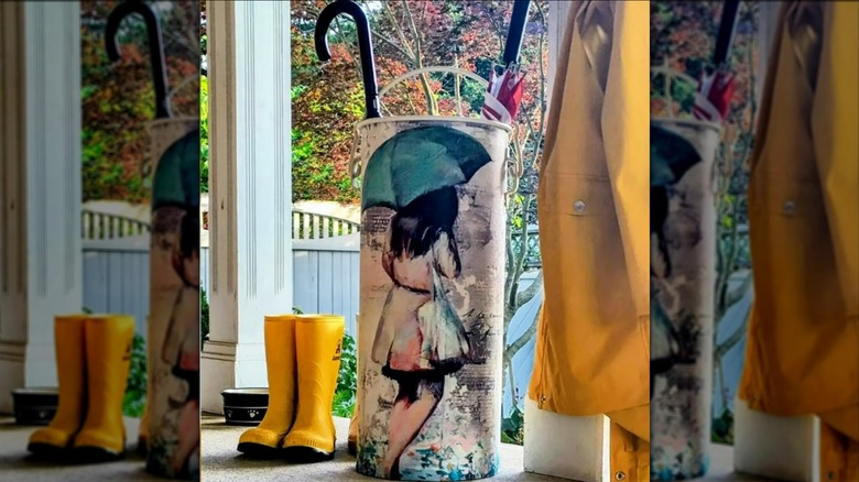 Decoupaged milk can with umbrellas in it next to rain boots and rain coat