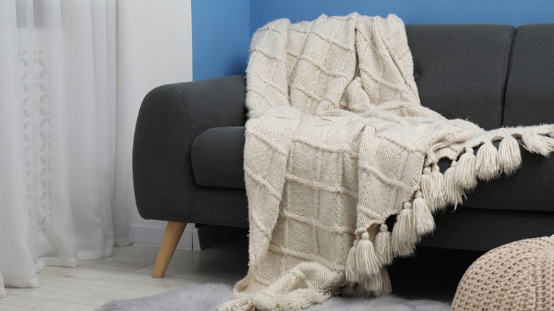 A white knit blanket draped over the arm of a couch