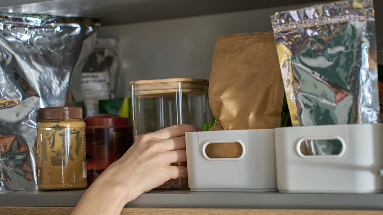 A hand reaching for items on a kitchen shelf