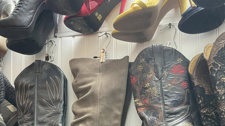 Boots hanging from pant clips on nails hammered into the wall of a closet.