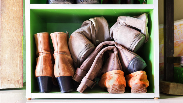 Shoes and boots stuffed into a small cubby in the bottom of a shelving unit.