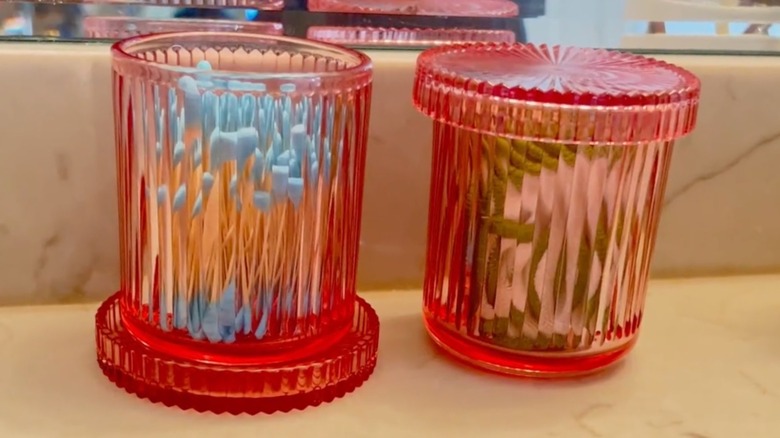 Two pink fluted glass jars holding cotton swabs on countertop