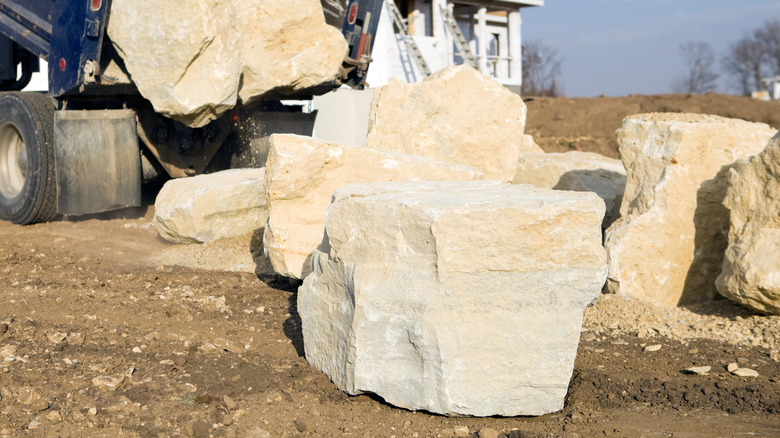 Large boulders on the building site of a new home with construction machinery in the background.