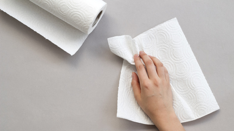 A hand wiping a surface with a paper towel.