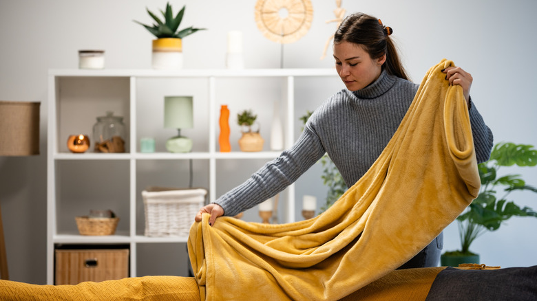 Woman standing behind couch folding yellow blanket