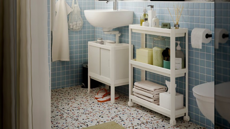 IKEA catalogue photo showing a white bathroom utility cart on wheels against blue tile wall