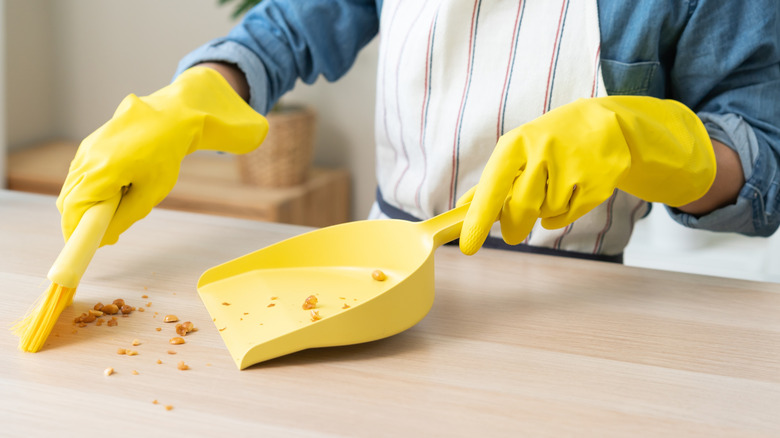 Gloved hands brushing crumbs off table into dust pan.