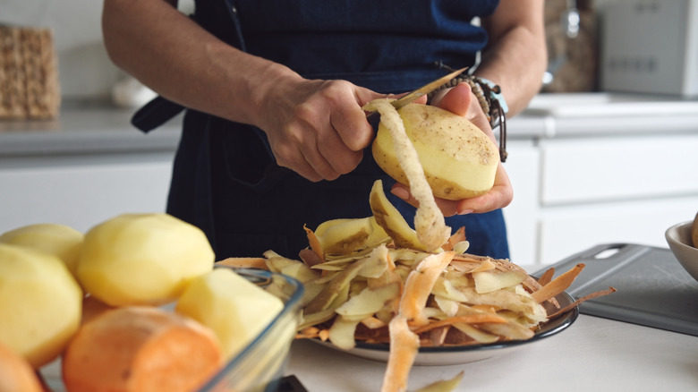 Person peeling potato skin into scrap bowl.