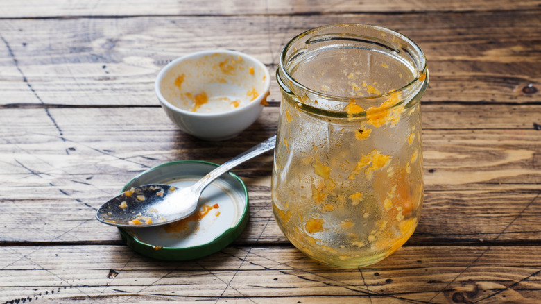 A mostly empty jar of fruit preserves sitting next to a dirty spoon on a lid.