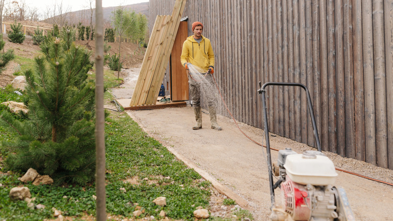 Man spraying water hose onto recently tilled gravel path preparing to install pavers.