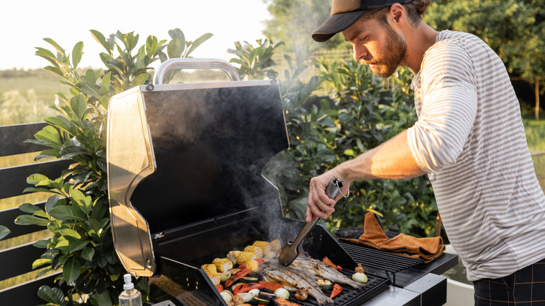 A person cooking fish and vegetables on a gas grill